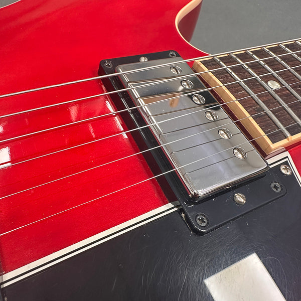 Close-up of electric guitar chrome pickup and strings on red and black body with white trim at Coffee House Guitars product listing