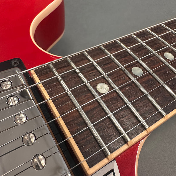 Close-up of red electric guitar fretboard with metal frets, pearl dot inlays, and chrome pickup screws at Coffee House Guitars