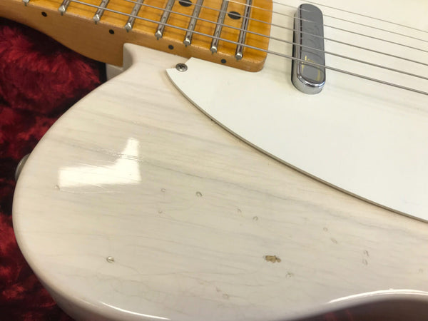 Close-up of white electric guitar body showing natural wood grain and light wear near neck joint and chrome pickup.