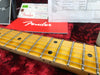 Close-up of Fender guitar maple fretboard with black dot inlays and metal frets on red plush case lining, accompanied by Fender owner's manual and paperwork.