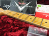 Close-up of Fender Custom Shop guitar maple neck and fretboard with metal frets and dot inlays, resting on plush red guitar case lining, showing Fender Custom Shop logo card and warranty paperwork in the background.