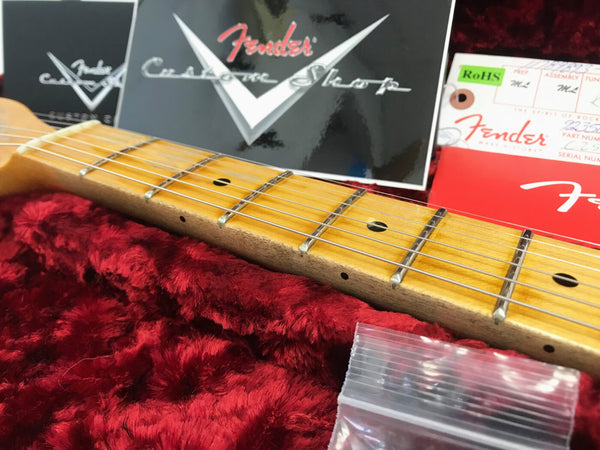 Close-up of Fender Custom Shop guitar maple neck and fretboard with metal frets and dot inlays, resting on plush red guitar case lining, showing Fender Custom Shop logo card and warranty paperwork in the background.