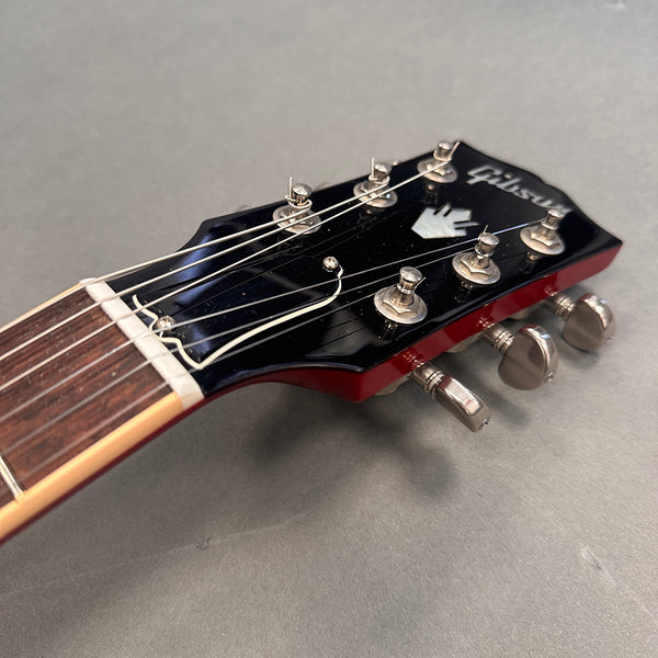 Close-up of Gibson electric guitar headstock with tuning pegs and strings on gray background
