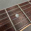 Close-up image of brown rosewood guitar fretboard with metal frets, six steel strings, and white dot inlay on second fret
