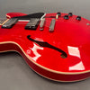 Close-up of bright red semi-hollow electric guitar body with f-hole, black pickguard, chrome bridge, and black control knobs on gray background