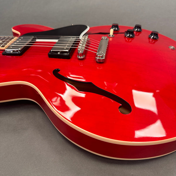 Close-up of bright red semi-hollow electric guitar body with f-hole, black pickguard, chrome bridge, and black control knobs on gray background