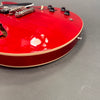 Close-up of red semi-hollow body electric guitar with cream binding and black control knobs on gray background