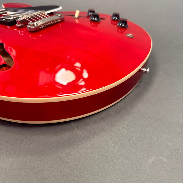 Close-up of red semi-hollow body electric guitar with cream binding and black control knobs on gray background