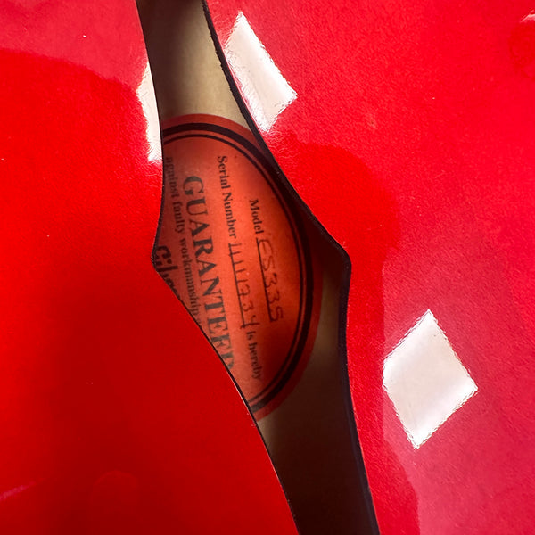 Close-up of the red glossy finish and soundhole label inside a Gibson ES-335 semi-hollow electric guitar showing the serial number and guarantee label.