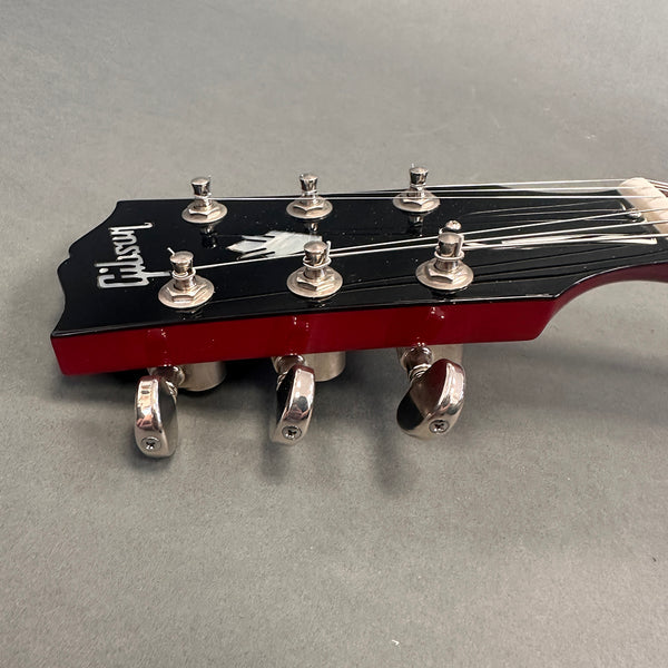 Close-up of Gibson guitar headstock with tuning pegs and strings on gray background