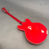 Back view of glossy red semi-hollow electric guitar with chrome tuning pegs and cream binding on a gray background
