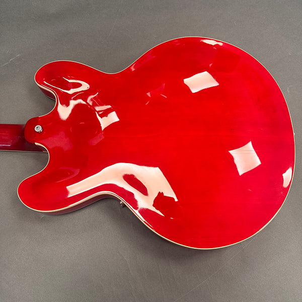 Back view of a glossy red semi-hollow electric guitar body with cream binding on a gray surface