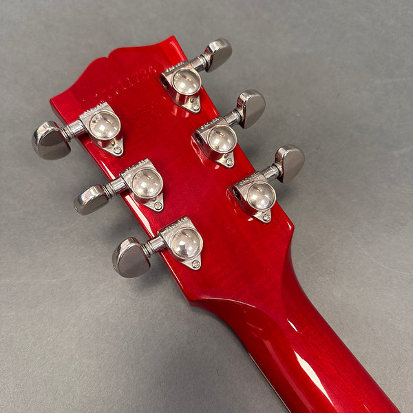 Back view of red guitar headstock with six chrome tuning pegs on gray background