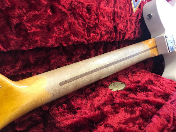 Close-up view of guitar neck with a skunk stripe wood pattern resting inside a plush red guitar case with G&G logo badge visible