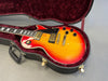 Electric guitar with sunburst finish in open black hardshell case with red velvet interior, showing black pickguard and control knobs