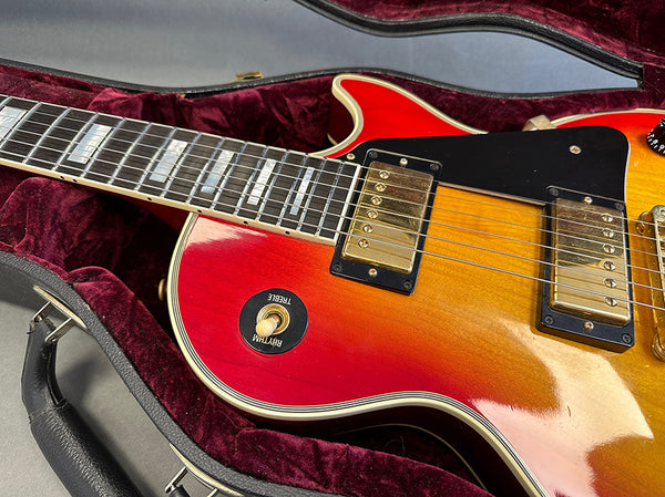 Close-up of vintage sunburst electric guitar body with gold humbucker pickups and rhythm/treble switch resting in plush red-lined hard case