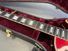 Close-up of electric guitar fretboard with rectangular pearl inlays inside red velvet-lined black hard case at Coffee House Guitars.