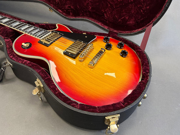 Sunburst electric guitar with dual humbucker pickups in a plush red-lined hard case, close-up of body and bridge.