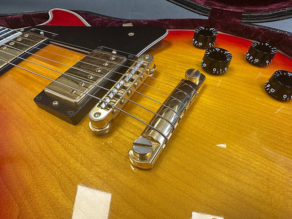 Close-up of sunburst electric guitar body showing bridge, tailpiece, humbucker pickup, volume and tone control knobs, and strings in velvet-lined case