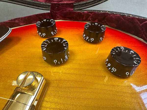 Close-up of sunburst electric guitar body showing black control knobs with white numbers and gold hardware in protective case.
