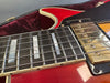 Close-up of red electric guitar neck showing mother-of-pearl rectangular fret inlays, steel strings, and gold humbucker pickup on black pickguard