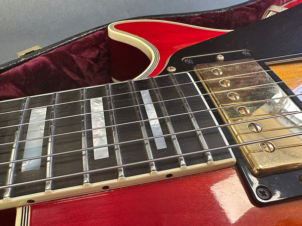 Close-up of red electric guitar neck showing mother-of-pearl rectangular fret inlays, steel strings, and gold humbucker pickup on black pickguard