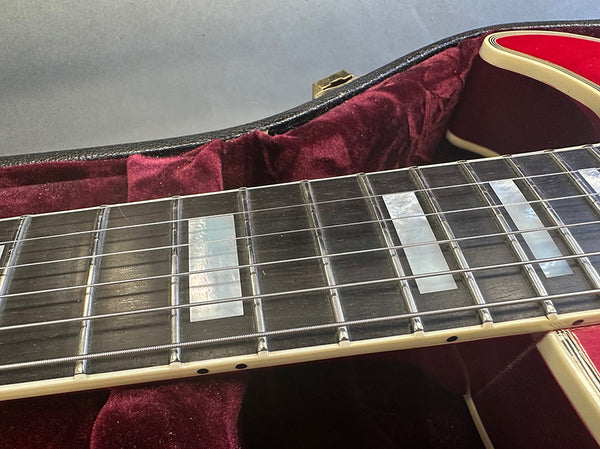 Close-up of electric guitar fretboard with rectangular mother of pearl inlays and metal frets, resting in plush red velvet guitar case.