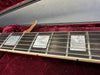 Close-up of guitar fretboard with mother of pearl block inlays and metal strings on dark wood fingerboard, resting in plush red guitar case interior.