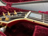 Close-up of black and red Les Paul Custom electric guitar headstock with gold tuning pegs and strings, resting in red velvet guitar case interior