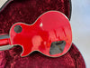Back of red electric guitar with glossy finish and black control cavity covers inside open guitar case with red plush lining