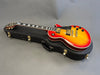 Sunburst electric guitar with gold hardware and humbucker pickups resting on black hard guitar case on grey background