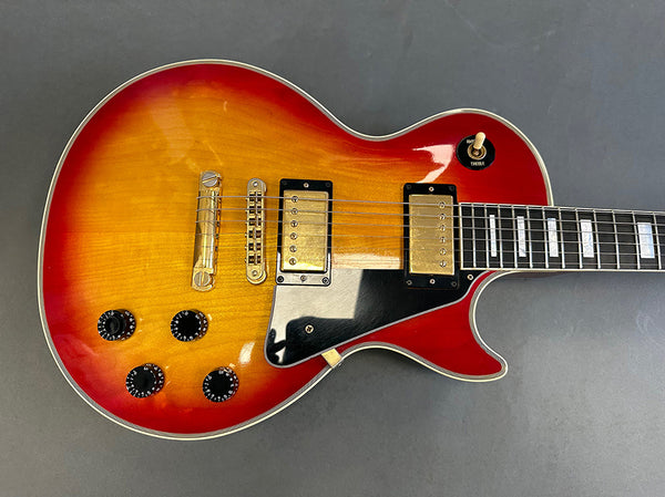 Close-up of sunburst electric guitar body featuring dual humbucker pickups, black pickguard, four control knobs, and toggle switch on gray background