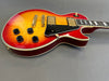 Cherry sunburst electric guitar with black pickguard and gold hardware on gray background