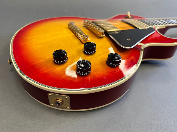 Close-up of red sunburst electric guitar body with black control knobs and gold hardware on gray background