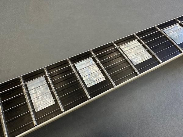Close-up of electric guitar fretboard with pearl block inlays and metal frets on dark wood fingerboard
