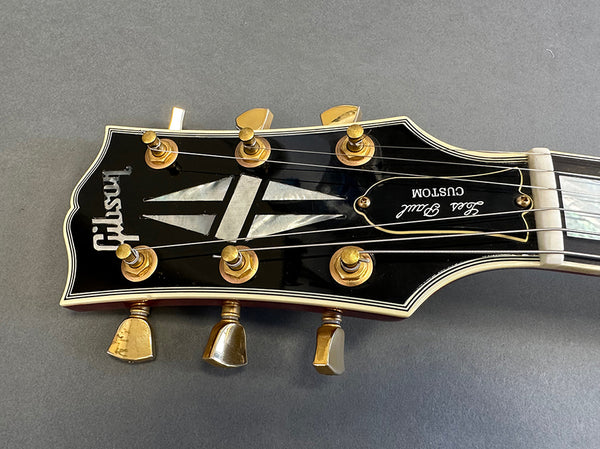 Close-up of Gibson Les Paul Custom guitar headstock with gold tuning pegs and mother-of-pearl inlay on gray background