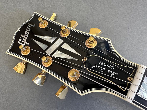Close-up of Gibson Les Paul Custom guitar headstock with gold tuning pegs and black finish