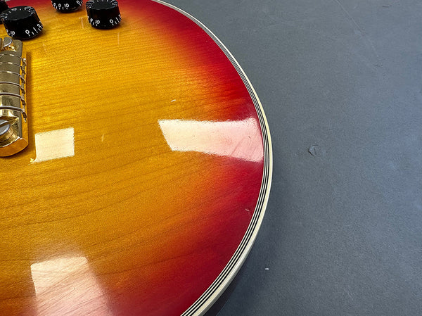 Close-up of sunburst finish electric guitar body with black control knobs and chrome bridge on gray background