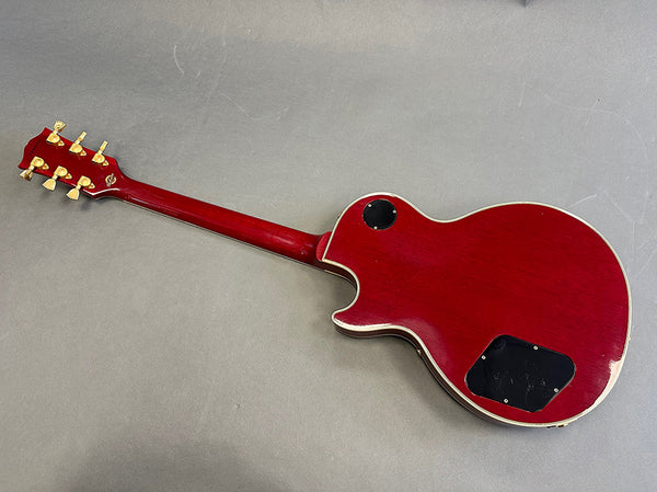 Back view of red solid body electric guitar with gold tuning pegs and cream binding on a gray surface