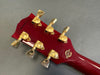 Close-up of red Gibson Custom Shop guitar headstock with gold tuning pegs and serial number on gray background