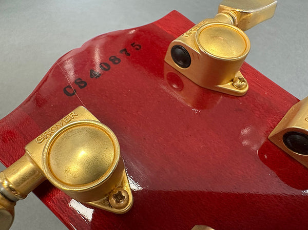 Close-up of red guitar headstock with gold Grover tuning pegs and serial number CS40875 stamped on the back.