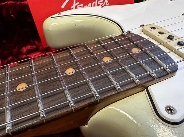 Close-up of Fender electric guitar rosewood fretboard and white body with vintage wear, displayed on red plush background