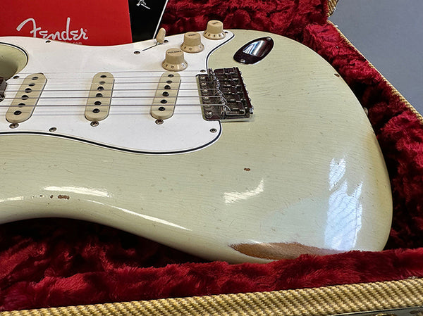 Close-up of vintage Fender Stratocaster electric guitar body in worn white finish with three single-coil pickups and white pickguard in red plush-lined guitar case