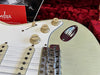 Close-up of vintage Fender Stratocaster electric guitar controls showing volume and tone knobs, white pickguard, and bridge with metal saddles, resting on red plush guitar case lining