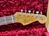 Close-up of Fender Stratocaster guitar headstock with vintage tuning pegs on red plush guitar case lining