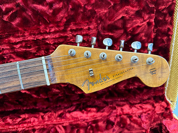 Close-up of Fender Stratocaster guitar headstock with vintage tuning pegs on red plush guitar case lining