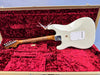 Vintage white electric guitar with maple neck in open red velvet-lined guitar case against blue background
