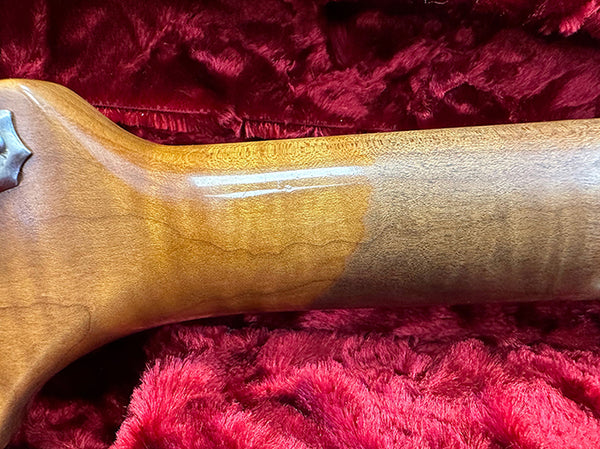 Close-up of polished guitar neck heel and back wooden grain resting on red plush fabric case interior