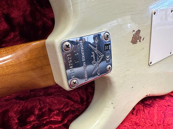 Close-up of Fender Limited Edition electric guitar neck plate with serial number on a vintage white guitar body resting on a red plush surface