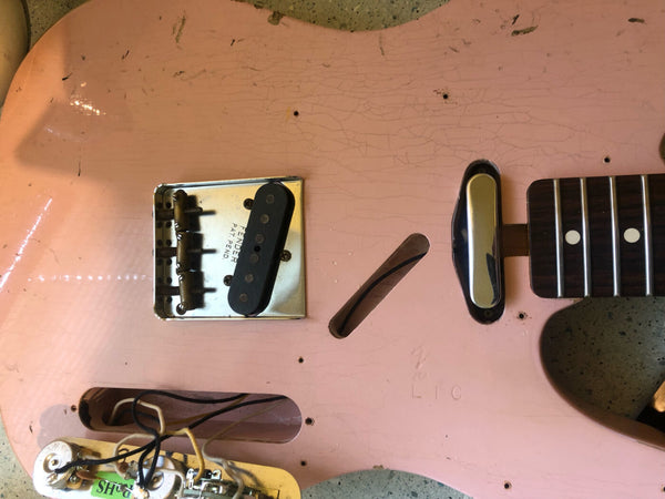 Close-up of vintage pink Fender guitar body showing bridge, pickup, and wiring cavity with aging and finish cracking detail